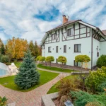 Abri de piscine bas en 2026 : moins de feuilles, pas de bassin autonome Tudor-style home with landscaped garden and pool under a vibrant cloudy sky.