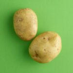 Pomme de terre Bintje : planter de mars à mai, récolter en 100 à 110 jours, sans jouer avec le gel Two fresh potatoes on a vibrant green background, perfect for food-related themes.